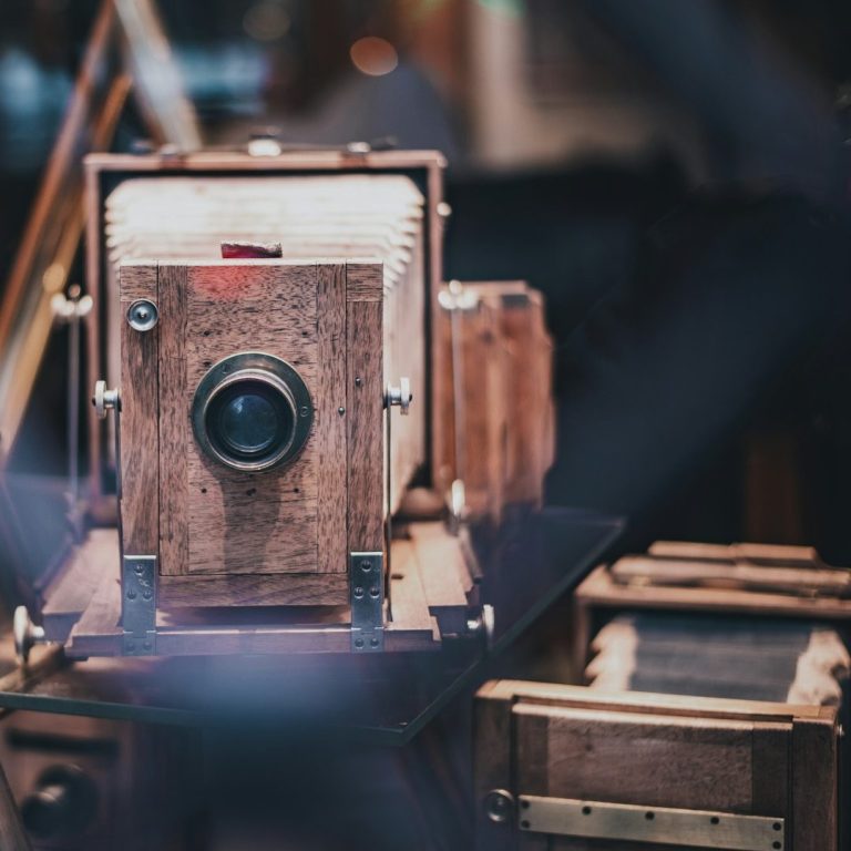 Antique wooden camera with a large lens, surrounded by vintage camera equipment.