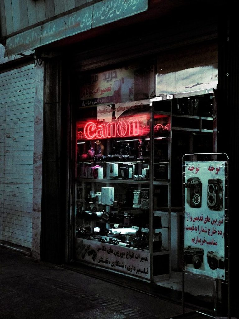 A shopfront displaying electronics with a neon "Open" sign and illuminated products inside.